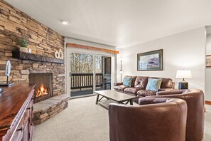 Una sala de estar con chimenea de piedra, muebles de cuero y vistas a través de un ventanal.