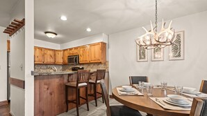 A modern kitchen with wooden cabinets, granite countertops, and a dining area with a round table and chairs. - Snow Flower 149 2 Bedroom Condo by RedAwning (Park City)