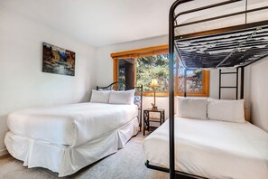 A bedroom with two single beds, a window with a view of trees, a painting on the wall, and a small table with a lamp. - Snow Flower 006 2 Bedroom Condo by RedAwning (Park City)