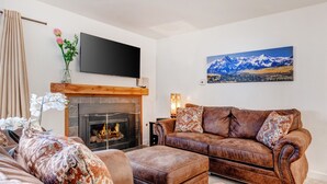 A living room with a fireplace, a brown leather sofa, and a flat-screen TV mounted on the wall.