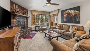 A living room with a fireplace, comfortable seating, a television, and a large painting. - Snow Flower 056 3 Bedroom Condo by RedAwning (Park City)