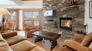 A cozy living room with a stone fireplace, comfortable seating, and a television mounted above it. - Snow Flower 074 3 Bedroom Condo by RedAwning (Park City)