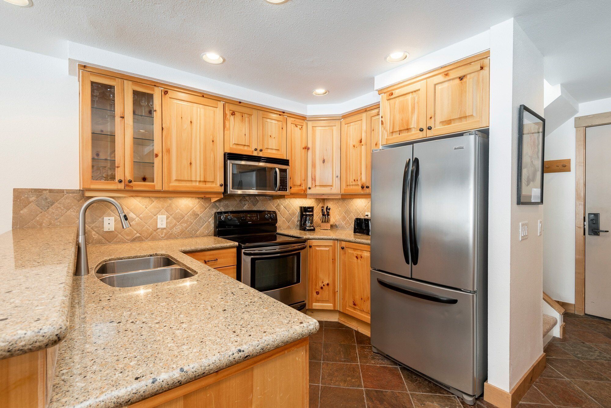 A kitchen with wooden cabinets, stainless steel appliances, granite countertops, and a tiled backsplash.