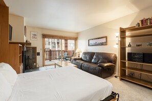 Et hotelværelse med en stor seng, en lædersofa, en træbogreol og en skydedør til en balkon.