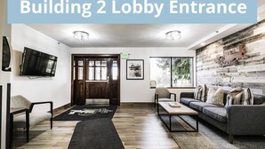 A modern living room with a wooden floor, a sofa, a coffee table, a TV, and a large window with a view of trees. - Park Station 233 2 Bedroom Condo by RedAwning (Park City)
