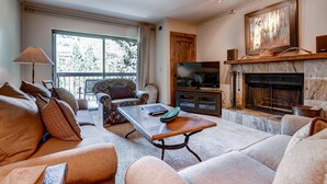 A living room with a sofa, armchair, and a coffee table. There is a fireplace with a TV above it. - Park Station 233 2 Bedroom Condo by RedAwning (Park City)