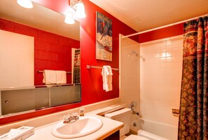 A bathroom with a red wall, a white sink, a mirror, a shower, and a poster.