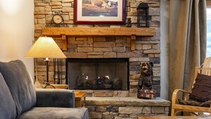 A cozy living room with a stone fireplace, a sofa, a wooden coffee table, and a lamp. - Snow Flower 023 2 Bedroom Condo by RedAwning (Park City)