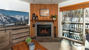 A living room with a fireplace, wooden paneling, a television, and a view of a deck with outdoor furniture.