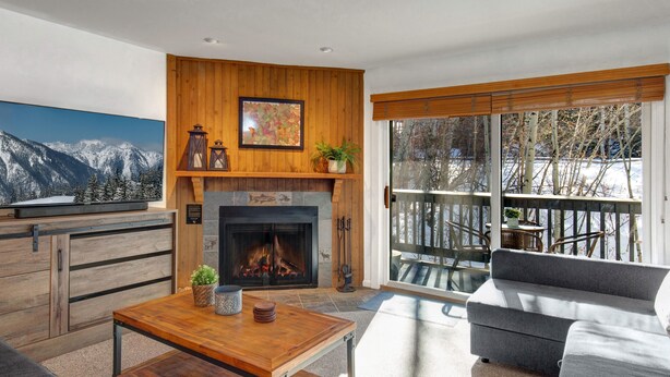 A living room with a fireplace, a large window with a view of trees, and a sofa.
