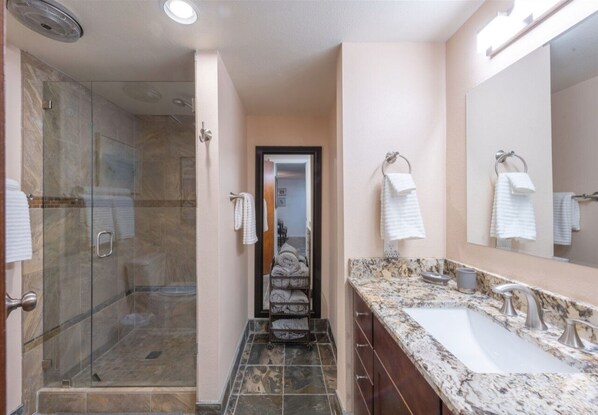 Un baño moderno con ducha envuelta en vidrio, lavamanos de mármol y un espejo grande.
