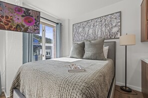 A bedroom with a large bed, a window with curtains, a painting on the wall, and a floor lamp. - Galleria 307-studio 1 Bedroom Home by RedAwning (Park City)