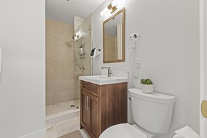A modern bathroom with a wooden vanity, a white sink, a toilet, and a glass shower enclosure. - Galleria 307-studio 1 Bedroom Home by RedAwning (Park City)