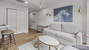 Un salon moderne avec un canapé gris, une table basse ronde et un tableau représentant un cheval accroché au mur.