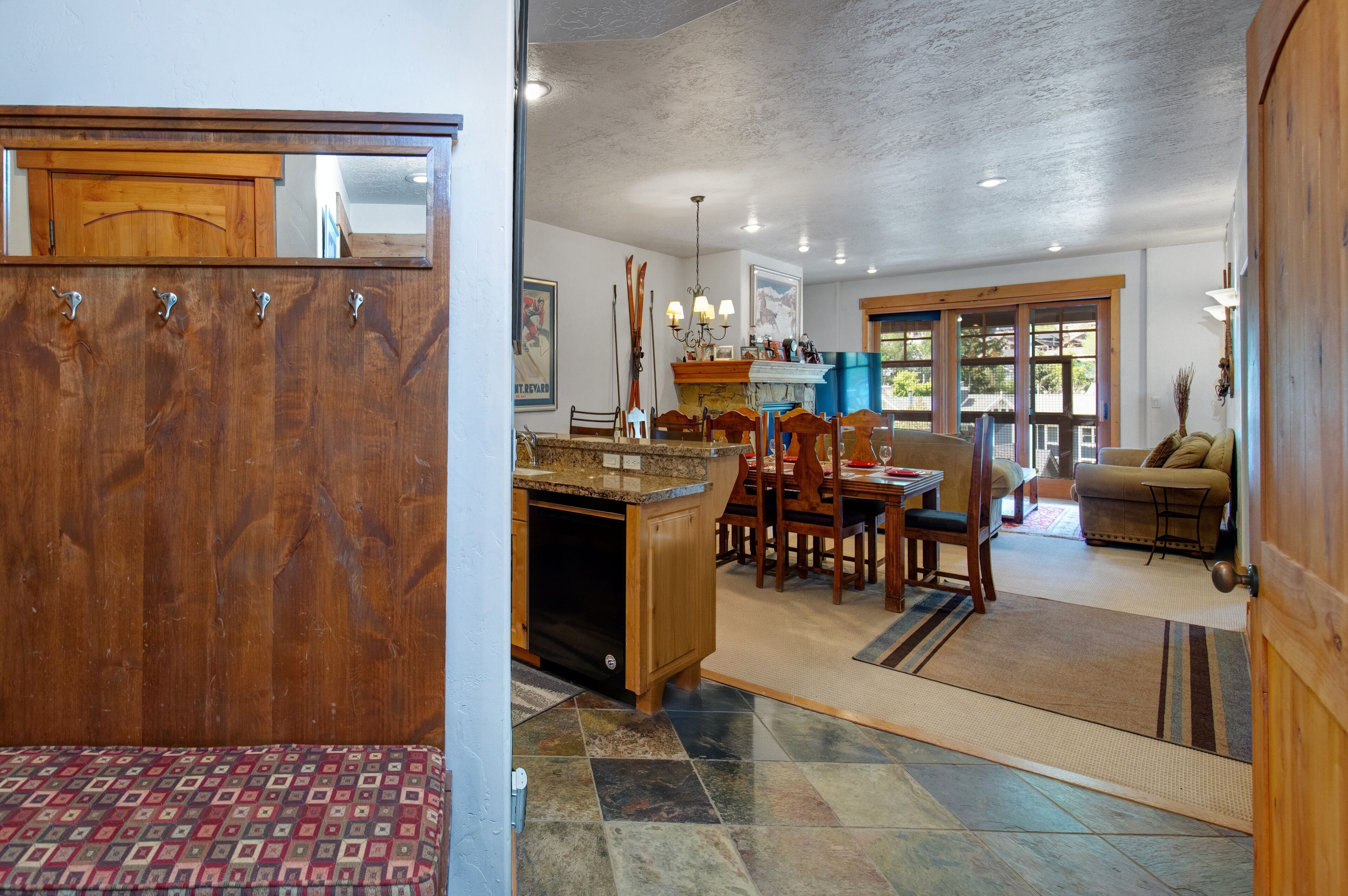 A spacious living area with a wooden dining table, chairs, and a sofa. There is a kitchen area with a granite countertop and wooden cabinets.