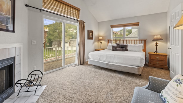 A bedroom with a bed, a chair, a nightstand, a lamp, a fireplace, and a balcony with a view.