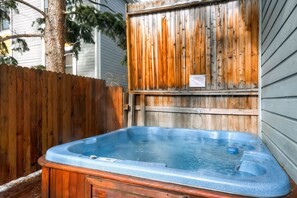 Un jacuzzi de madera en un patio trasero con un cerco de madera y una casa al fondo.
