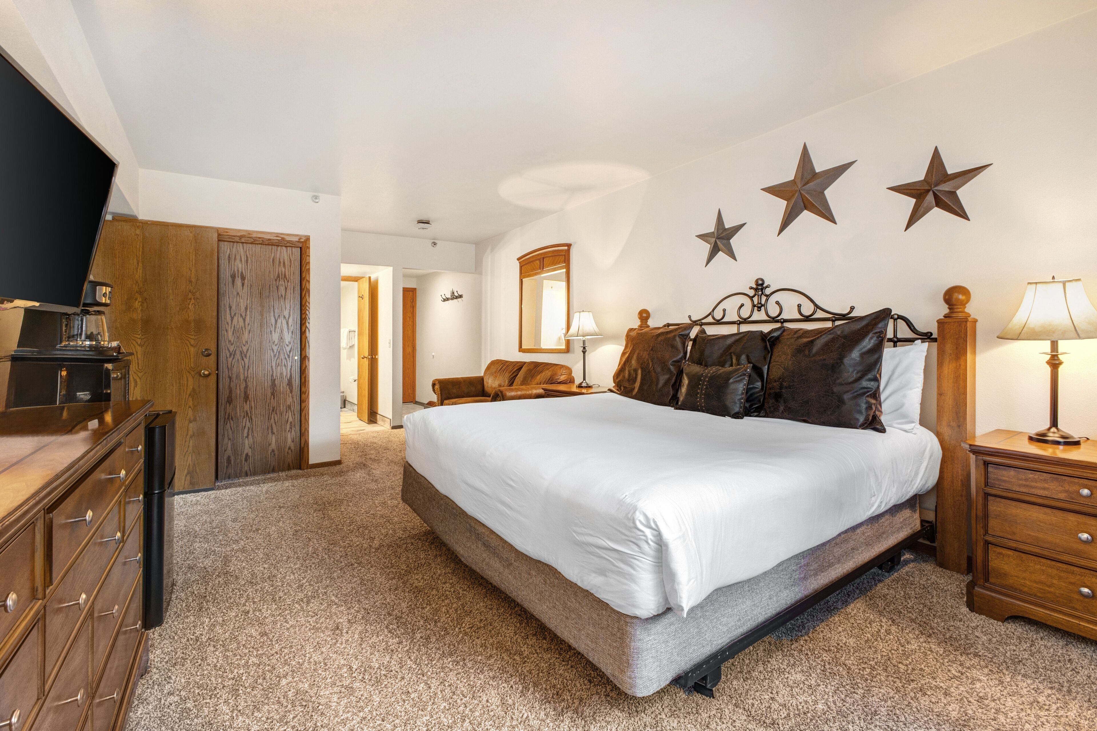 A bedroom with a large bed, wooden dresser, and a television on a stand.