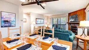 A dining area with a wooden table set for four, a fireplace, and a view of the outdoors. - Snow Flower 150 2 Bedroom Condo by RedAwning (Park City)