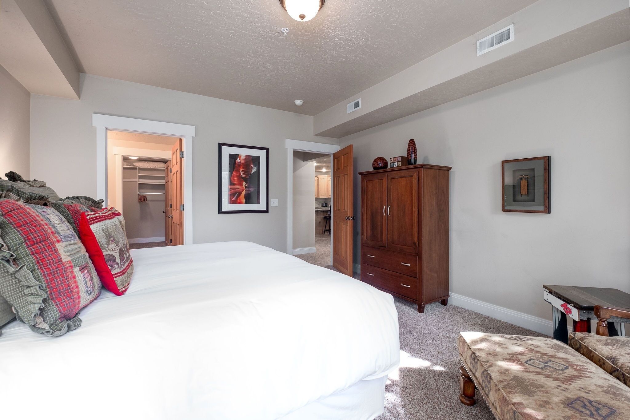 A bedroom with a large bed, a wooden wardrobe, and a small table. There is a closet with a door leading to another room.