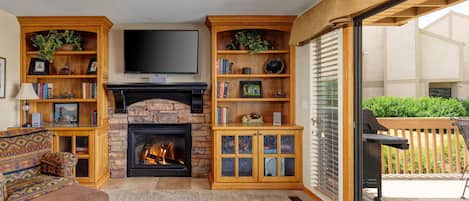 A cozy living room with a fireplace, wooden shelving, a sofa, and a television.