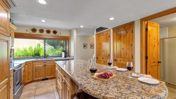 A kitchen with granite countertops, wooden cabinets, a large island, and a view of greenery outside. - Racquet Club 60 2 Bedroom Condo by RedAwning (Park City)