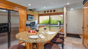 A kitchen with wooden cabinets, a stainless steel refrigerator, a granite countertop, and a large island with stools. - Racquet Club 60 2 Bedroom Condo by RedAwning (Park City)