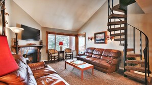 Ein geräumiges Wohnzimmer mit Ledersofas, einem Kamin, einem Fernseher und einer Wendeltreppe.