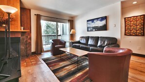 A living room with a fireplace, a sofa, a coffee table, and a large window with curtains. - Snow Flower 104 2 Bedroom Condo by RedAwning (Park City)