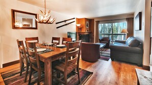 A dining area with a wooden table and chairs, a chandelier, and a fireplace. - Snow Flower 104 2 Bedroom Condo by RedAwning (Park City)