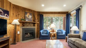 A cozy living room with a fireplace, two blue armchairs, a wooden coffee table, and a beige sofa. - Snow Flower 042 1 Bedroom Condo by RedAwning (Park City)
