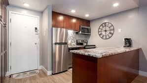 A modern kitchen with wooden cabinets, stainless steel appliances, and a large clock on the wall.