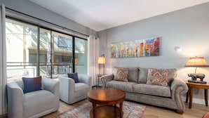 A modern living room with a large window, a sofa, two armchairs, a round wooden coffee table, and a painting on the wall.