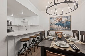 A modern kitchen with white cabinets, a dining area with a wooden table set for four, and a chandelier.