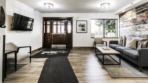 A modern living room with a wooden floor, a sofa, a coffee table, a TV, and a large window with a view of trees.