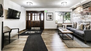 Uma sala de estar moderna com piso de madeira, um sofá, uma mesa de centro, uma televisão e uma grande janela com vista para árvores.