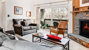 A living room with a fireplace, a sofa, a coffee table, and a view of the outdoors.