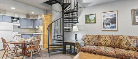 A compact living space with a spiral staircase, a dining area with wooden furniture, and a sofa with patterned cushions.