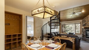 A dining area with a wooden table set for four, a spiral staircase, and a view of a snowy landscape through a window. - Snow Flower 038 3 Bedroom Condo by RedAwning (Park City)