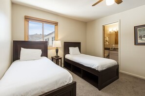 A hotel room with two single beds, a window with a view, a bathroom visible through an open door, and a ceiling fan. - Snow Flower 038 3 Bedroom Condo by RedAwning (Park City)