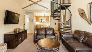 A spacious living area with leather sofas, a coffee table, a TV, and a spiral staircase. - Snow Flower 038 3 Bedroom Condo by RedAwning (Park City)