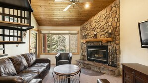 A cozy living room with a stone fireplace, leather sofas, a round coffee table, and a ceiling fan. - Snow Flower 038 3 Bedroom Condo by RedAwning (Park City)