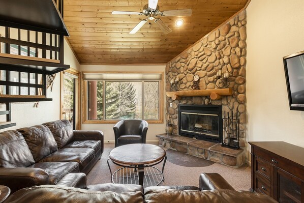 A cozy living room with a stone fireplace, leather sofas, a round coffee table, and a ceiling fan. - Snow Flower 038 3 Bedroom Condo by RedAwning (Park City)