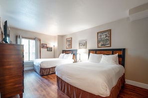 A hotel room with two beds, wooden flooring, a dresser, and framed pictures on the walls. - Park Station 111 1 Bedroom Condo by RedAwning (Park City)