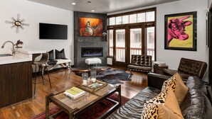 A modern living room with a fireplace, leather sofa, and a dining area with bar stools.