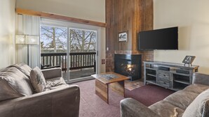 A living room with a fireplace, a television mounted on the wall, and a sliding glass door leading to an outdoor area. - Snow Flower 127 2 Bedroom Condo by RedAwning (Park City)