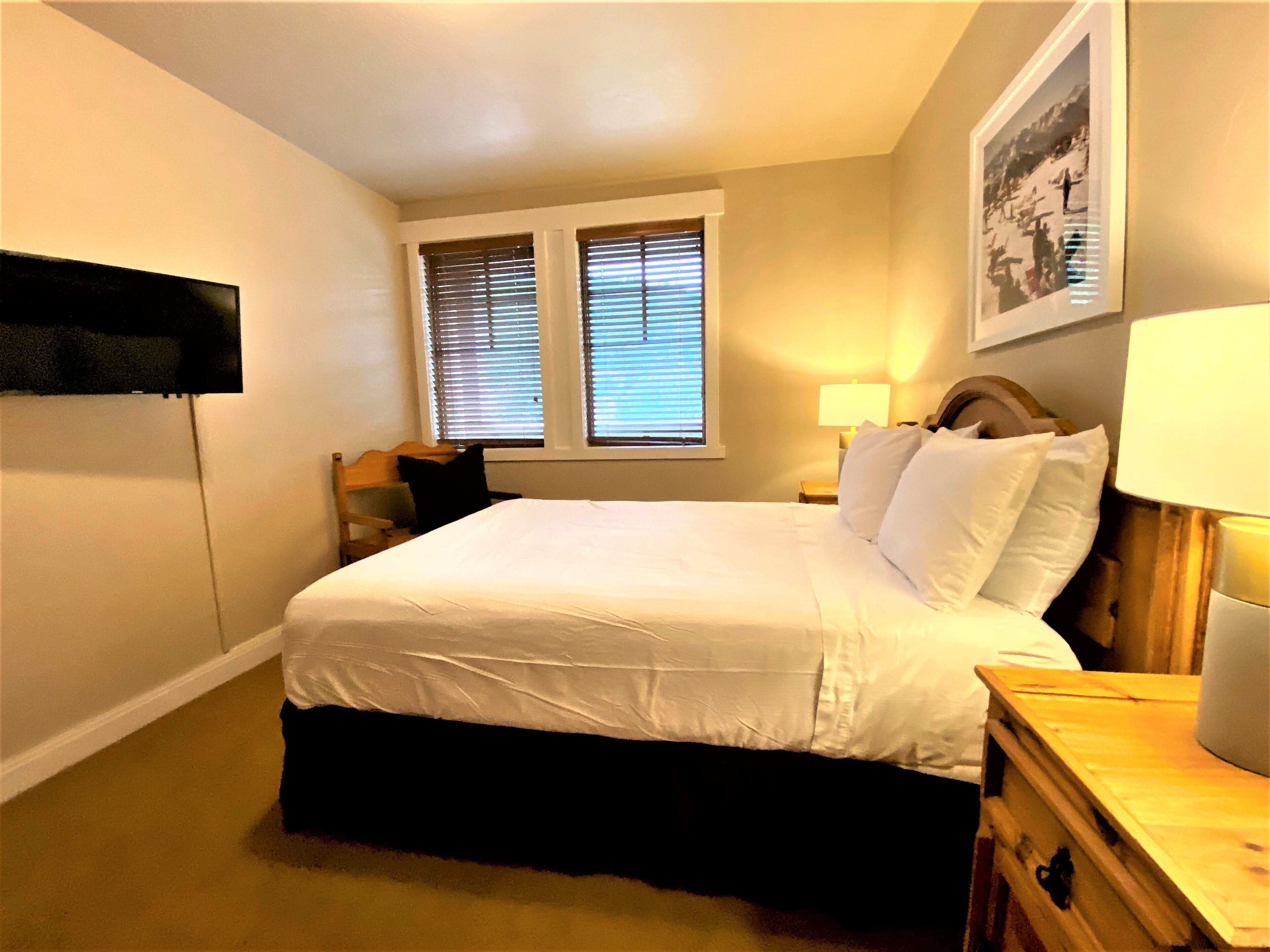 Une chambre à coucher avec un lit, deux tables de chevet, une commode, une lampe et un tableau au mur.