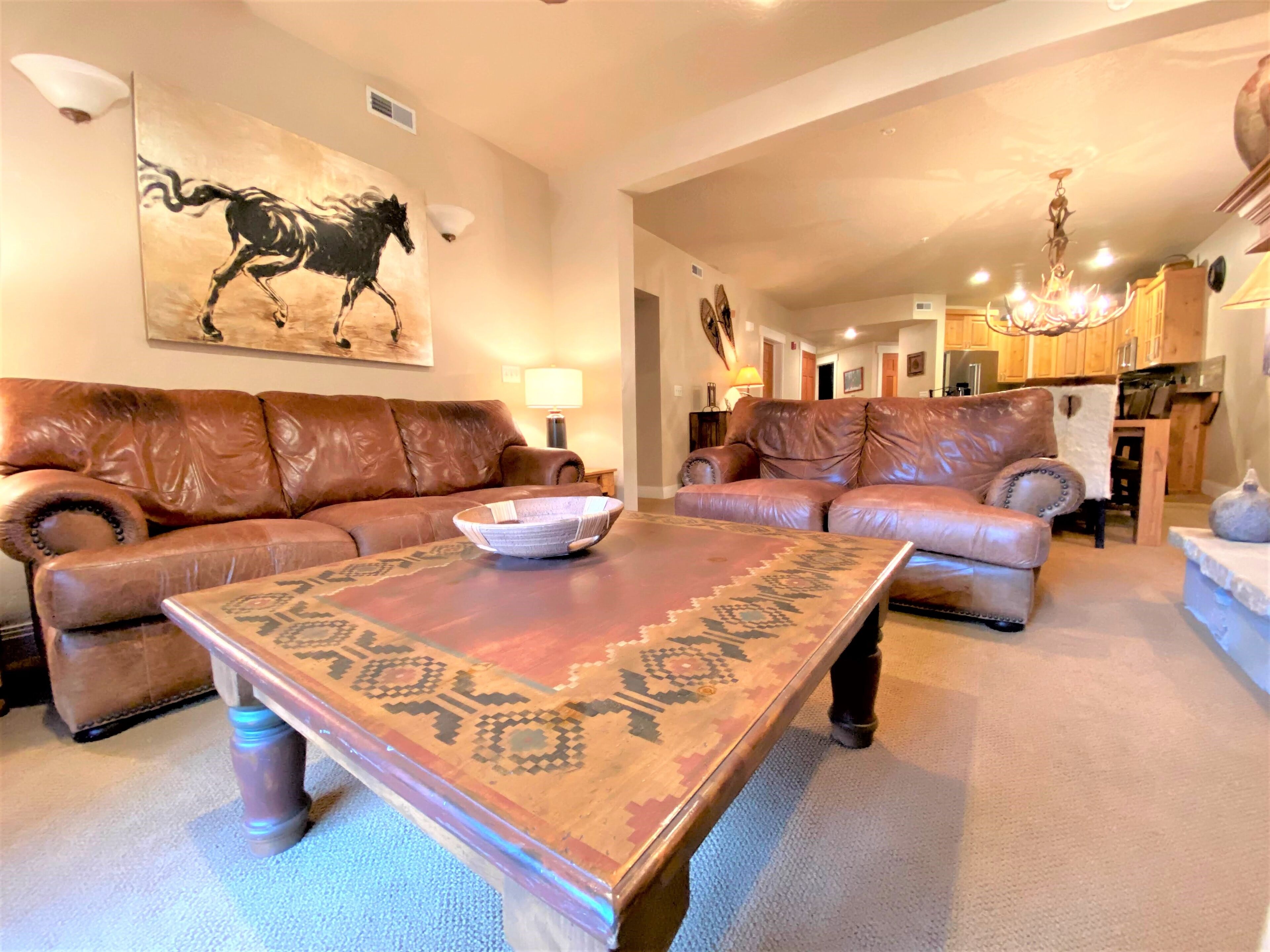 Ein geräumiges Wohnzimmer mit zwei Ledersofas, einem Couchtisch mit Muster und einem großen Gemälde von Pferden an der Wand.
