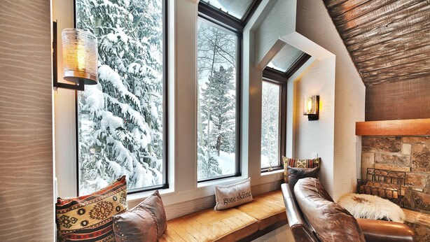 A cozy seating area with a bench and cushions, large windows with a snowy view, and a stone fireplace.