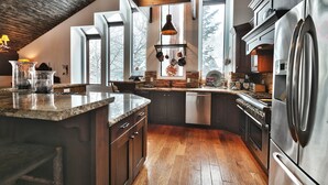 A modern kitchen with a wooden ceiling, large windows, and stainless steel appliances.